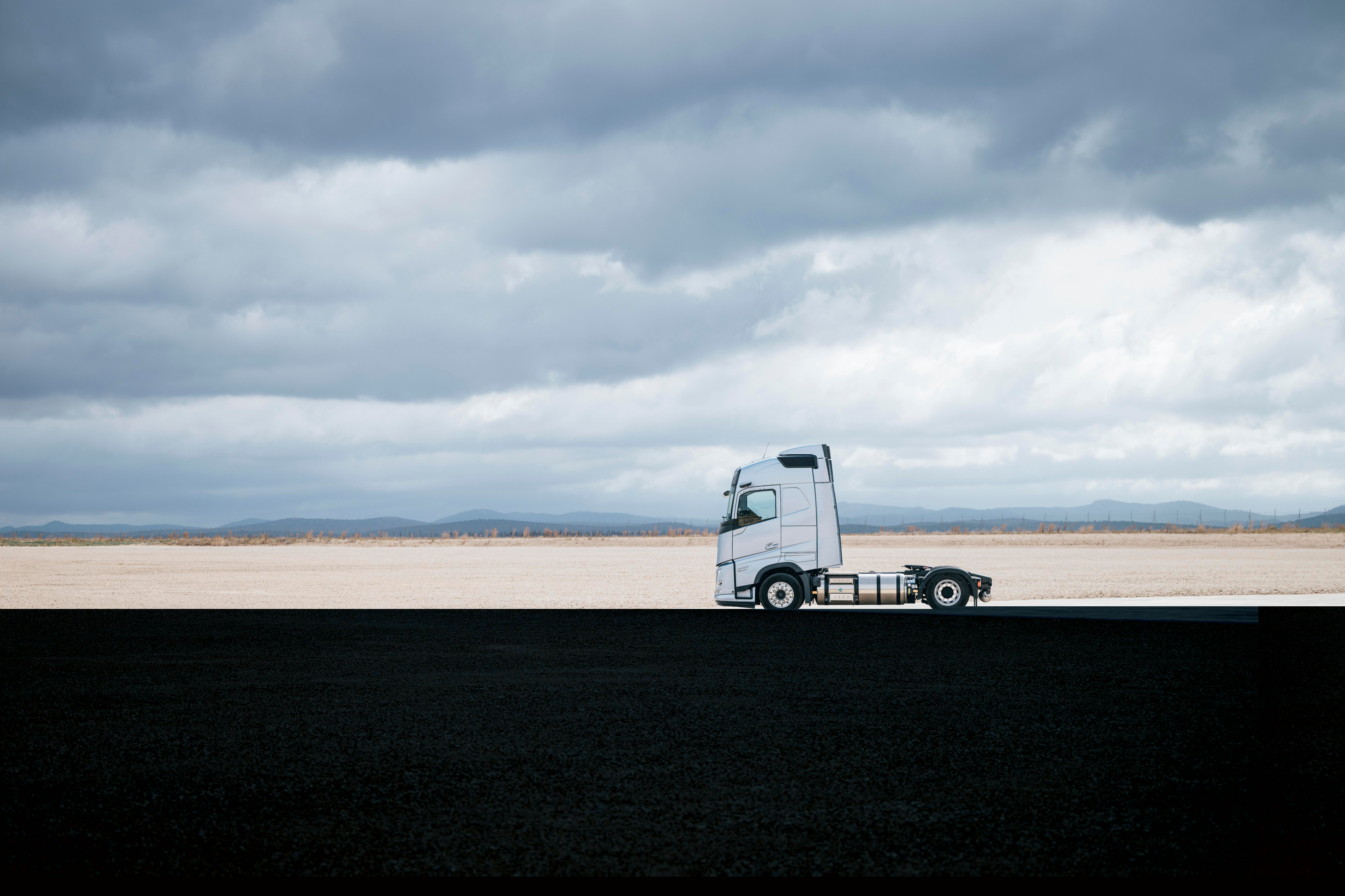 Side view of a Volvo truck parked on a wide, open landscape under a cloudy sky, with expansive surroundings and minimal scenery.